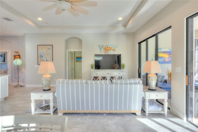 living room with a raised ceiling, ceiling fan, and plenty of natural light