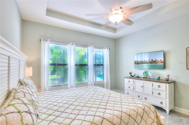 bedroom with light colored carpet, ceiling fan, and a tray ceiling