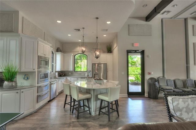 kitchen with stainless steel appliances, hardwood / wood-style flooring, white cabinets, a center island, and hanging light fixtures