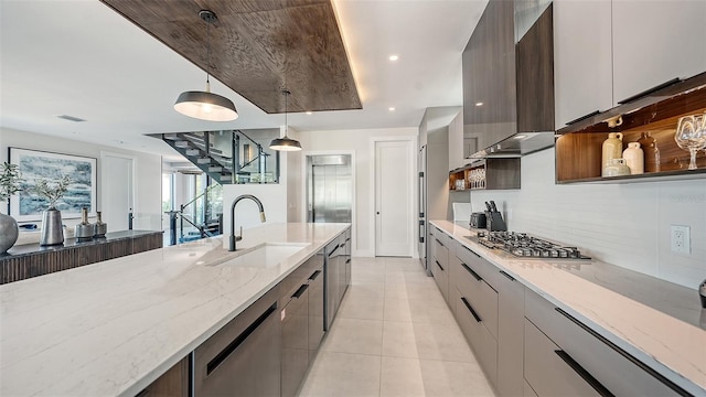 kitchen with wall chimney range hood, sink, light stone countertops, appliances with stainless steel finishes, and decorative light fixtures