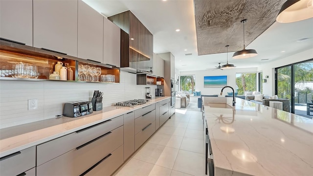 kitchen featuring backsplash, sink, ceiling fan, light stone countertops, and decorative light fixtures