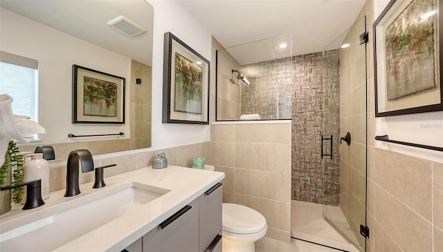 bathroom featuring vanity, tile patterned flooring, toilet, tile walls, and a shower with shower door