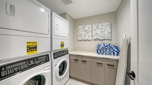 clothes washing area featuring washer and dryer, cabinets, light tile patterned floors, and stacked washer / dryer