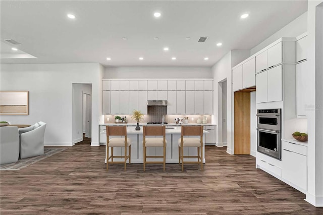 8007 Nevis Run, Bradenton, FL 34202 - kitchen with double oven, tasteful backsplash, white cabinetry, recessed lighting, and an island with sink