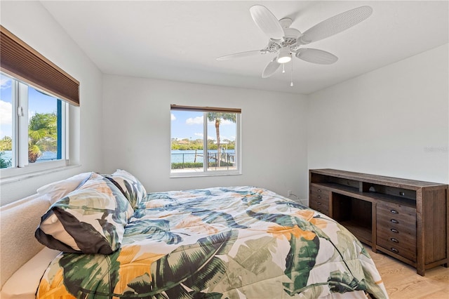 bedroom featuring light wood-type flooring, a water view, and ceiling fan