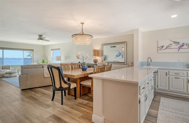 kitchen featuring sink, hanging light fixtures, a water view, white cabinets, and ceiling fan with notable chandelier