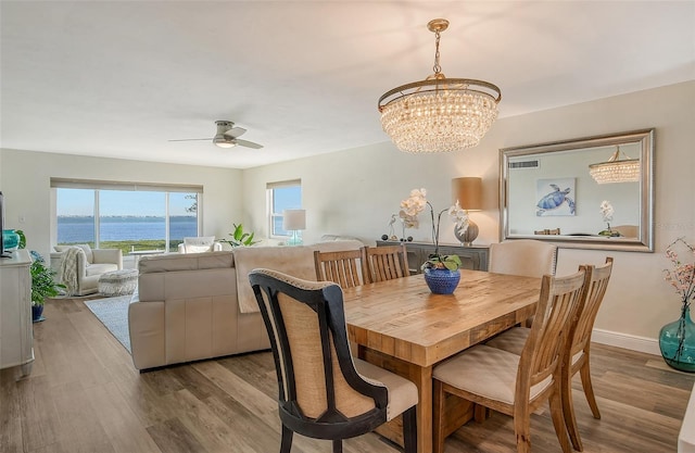 dining space featuring a water view, ceiling fan with notable chandelier, and light wood-type flooring