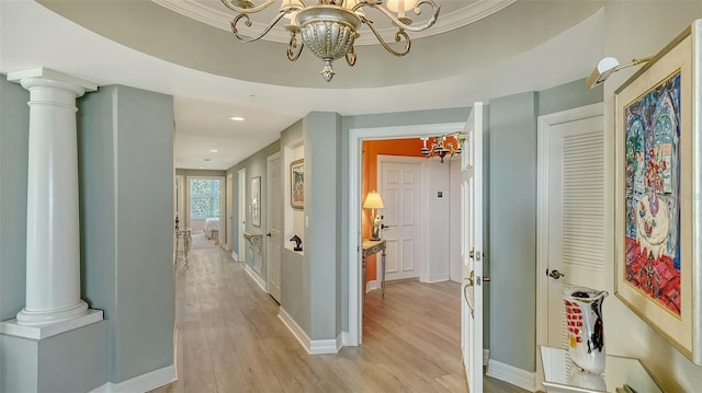 hall featuring ornate columns, ornamental molding, light wood-type flooring, and a notable chandelier