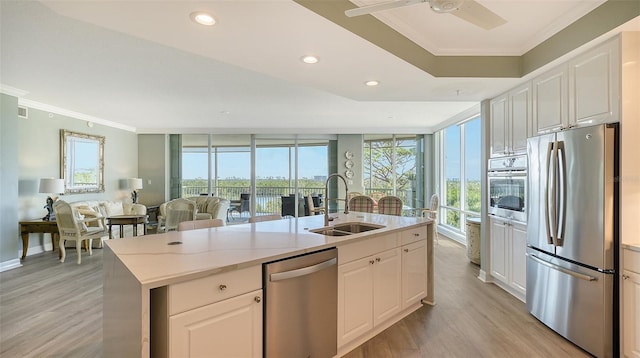 kitchen with white cabinetry, sink, stainless steel appliances, expansive windows, and a center island with sink