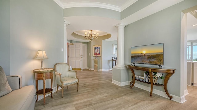 hallway with light wood-type flooring, decorative columns, an inviting chandelier, and ornamental molding