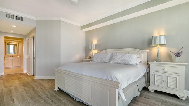 bedroom with connected bathroom, light hardwood / wood-style flooring, and crown molding