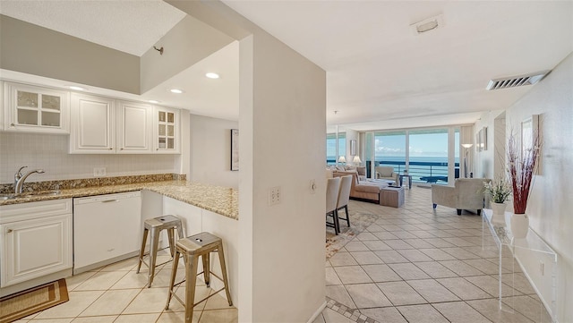 kitchen with white cabinetry, dishwasher, light stone countertops, sink, and light tile patterned floors