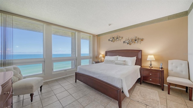 bedroom featuring light tile patterned floors, a water view, a view of the beach, and a textured ceiling