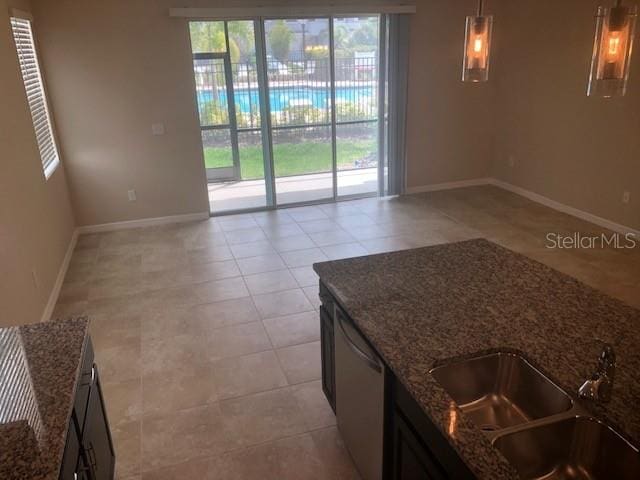 interior space featuring light tile patterned floors, sink, stainless steel dishwasher, and dark stone countertops