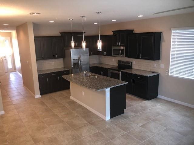 kitchen with pendant lighting, sink, an island with sink, light stone counters, and stainless steel appliances