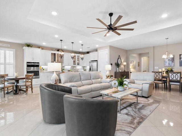 living room featuring ceiling fan with notable chandelier, a tray ceiling, light tile patterned flooring, and recessed lighting