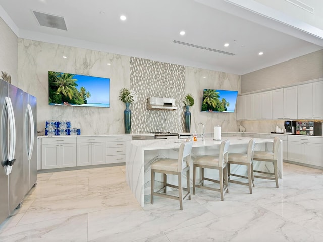 kitchen with freestanding refrigerator, white cabinets, a center island with sink, and a kitchen breakfast bar