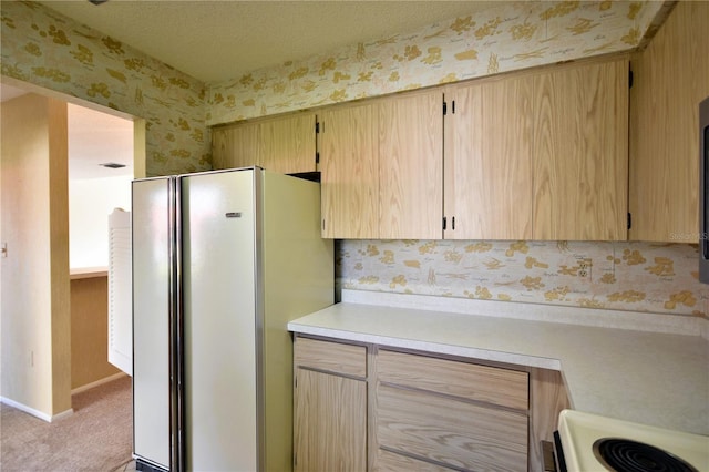 kitchen with a textured ceiling, light colored carpet, light brown cabinets, white refrigerator, and range