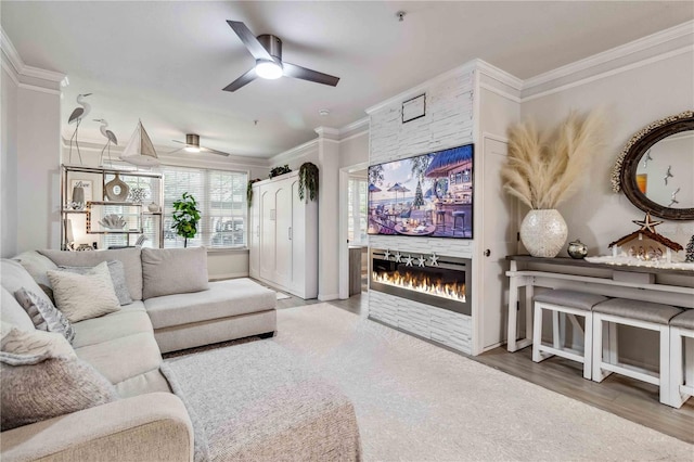 living area featuring a stone fireplace, a ceiling fan, and crown molding