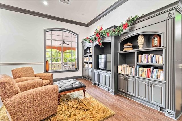 living area featuring light wood finished floors, visible vents, ornamental molding, and a ceiling fan