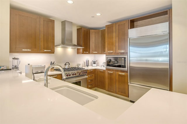 kitchen featuring built in appliances, sink, and wall chimney exhaust hood