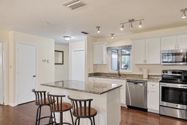 kitchen with white cabinets, sink, a kitchen island, light stone counters, and stainless steel appliances