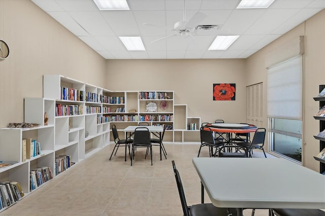 rec room with light tile patterned floors, a paneled ceiling, and ceiling fan