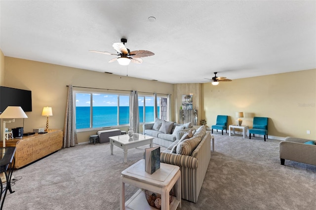 carpeted living room with ceiling fan and a water view