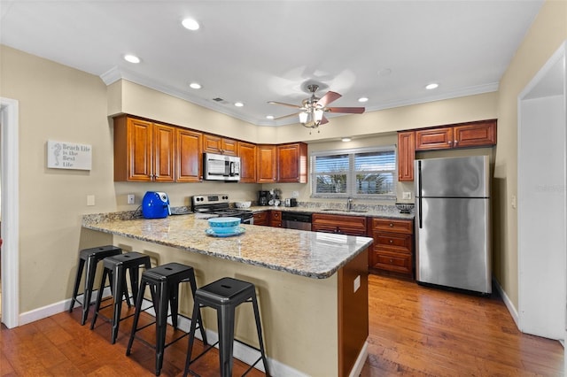 kitchen with light stone countertops, kitchen peninsula, stainless steel appliances, ceiling fan, and sink