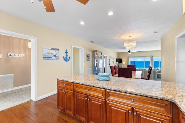 kitchen featuring light stone countertops, hardwood / wood-style floors, hanging light fixtures, and ceiling fan with notable chandelier