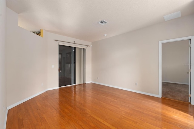 empty room with a textured ceiling and light hardwood / wood-style flooring