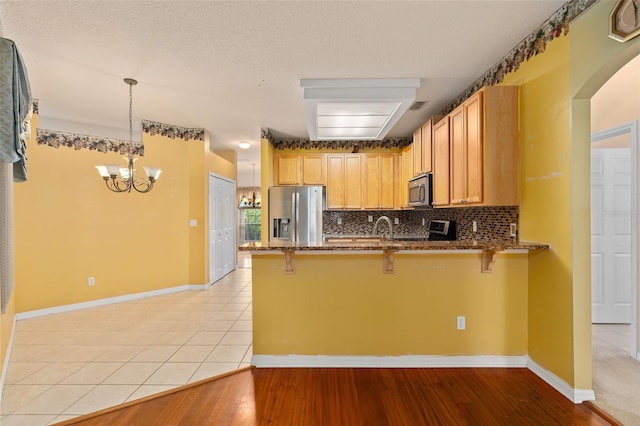 kitchen with kitchen peninsula, appliances with stainless steel finishes, light wood-type flooring, hanging light fixtures, and a breakfast bar area