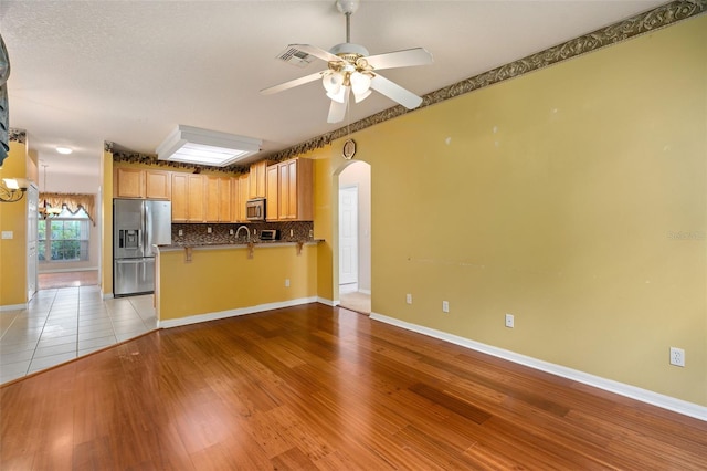 kitchen featuring ceiling fan, kitchen peninsula, light hardwood / wood-style floors, a breakfast bar, and appliances with stainless steel finishes