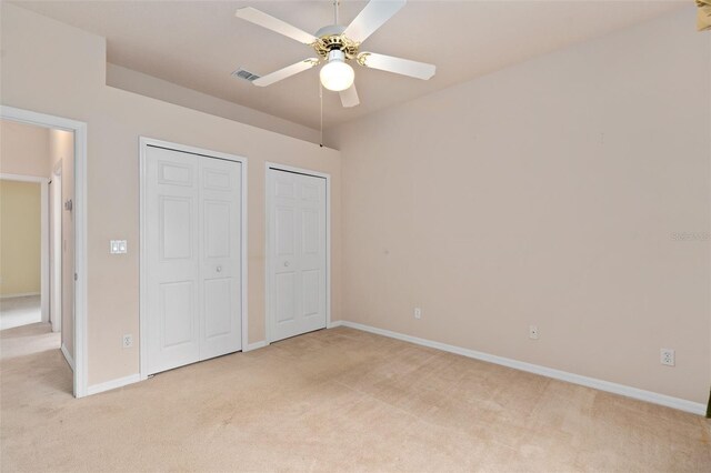 unfurnished bedroom featuring multiple closets, ceiling fan, and light carpet