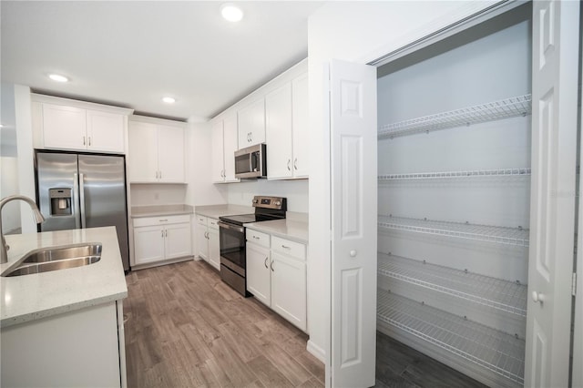 kitchen featuring light stone countertops, white cabinetry, sink, light hardwood / wood-style floors, and appliances with stainless steel finishes