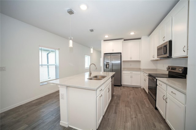 kitchen with appliances with stainless steel finishes, a kitchen island with sink, dark wood-type flooring, sink, and pendant lighting