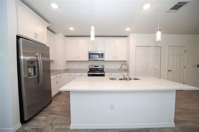 kitchen with hanging light fixtures, sink, appliances with stainless steel finishes, and an island with sink