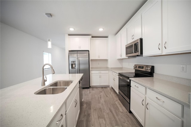 kitchen with sink, stainless steel appliances, light stone counters, pendant lighting, and light hardwood / wood-style floors