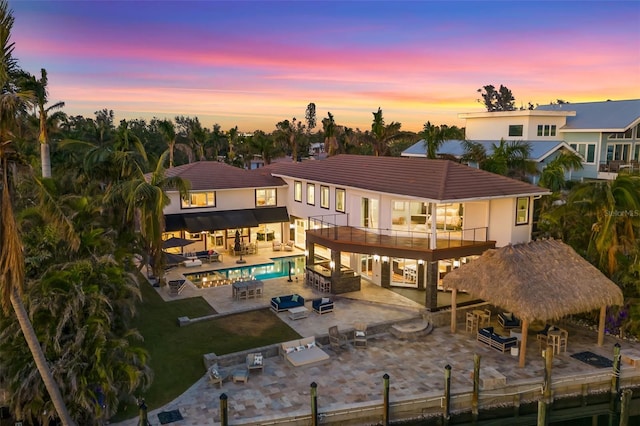 back house at dusk with a balcony, area for grilling, a pool with hot tub, a patio area, and a yard