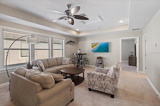 living room with a raised ceiling, ceiling fan, and light colored carpet