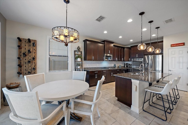 kitchen with hanging light fixtures, an inviting chandelier, decorative backsplash, a center island with sink, and appliances with stainless steel finishes