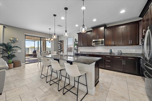 kitchen featuring appliances with stainless steel finishes, backsplash, sink, decorative light fixtures, and an island with sink