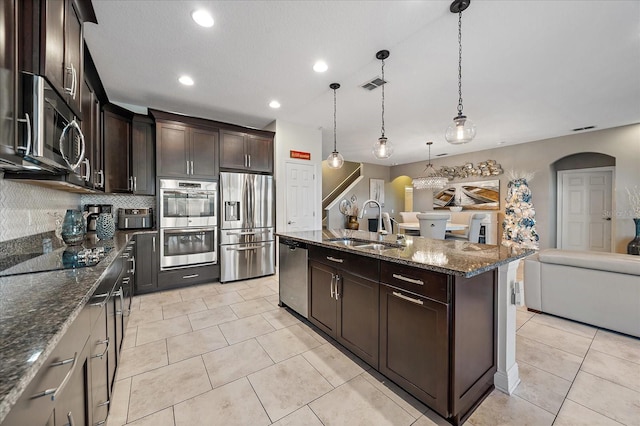 kitchen featuring pendant lighting, a center island with sink, sink, appliances with stainless steel finishes, and dark brown cabinets