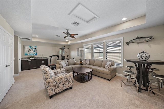 living room with a raised ceiling, ceiling fan, light colored carpet, and a textured ceiling