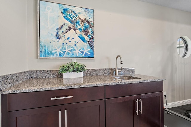 bar featuring dark brown cabinetry, light stone counters, and sink