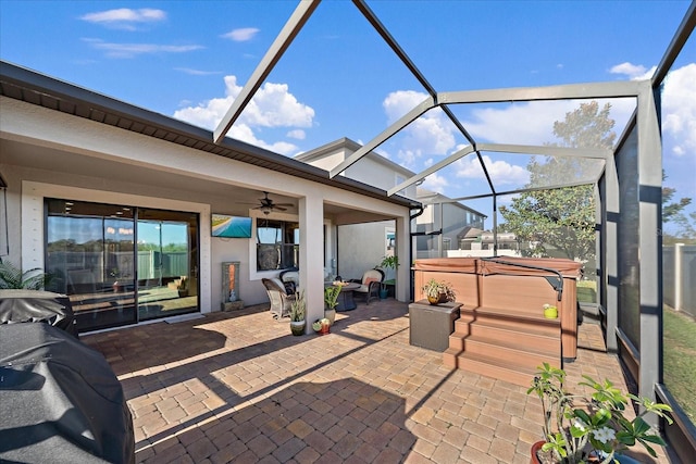 view of patio featuring glass enclosure, ceiling fan, and a hot tub