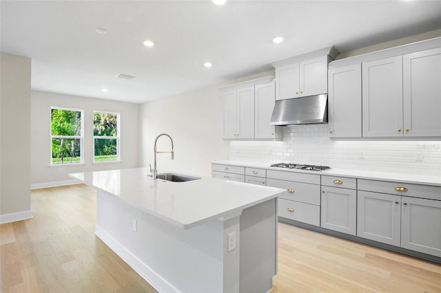 kitchen featuring sink, gas cooktop, light hardwood / wood-style floors, decorative backsplash, and a center island with sink