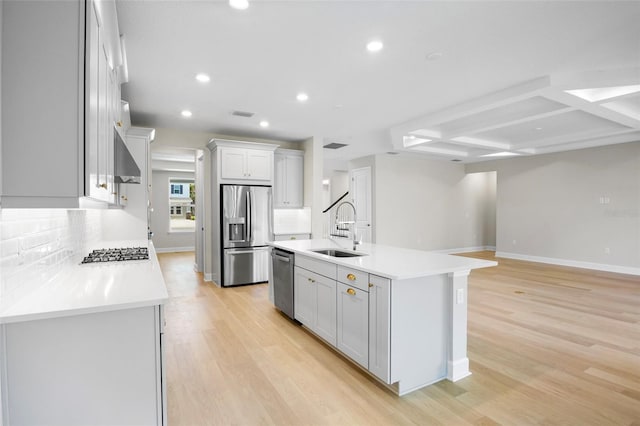 kitchen with sink, coffered ceiling, an island with sink, light hardwood / wood-style floors, and appliances with stainless steel finishes