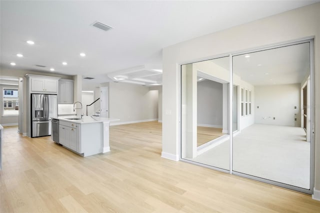 kitchen featuring sink, light hardwood / wood-style flooring, a kitchen island with sink, white cabinets, and appliances with stainless steel finishes