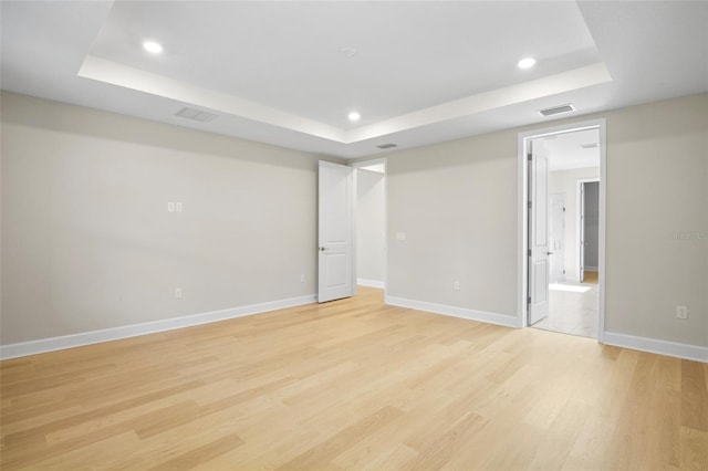 empty room featuring light wood-type flooring and a raised ceiling